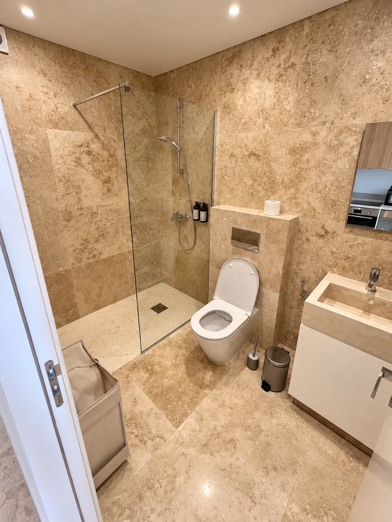 Avalon Gardens A002 bathroom with walk-in shower, WC and vanity in warm stone finishes